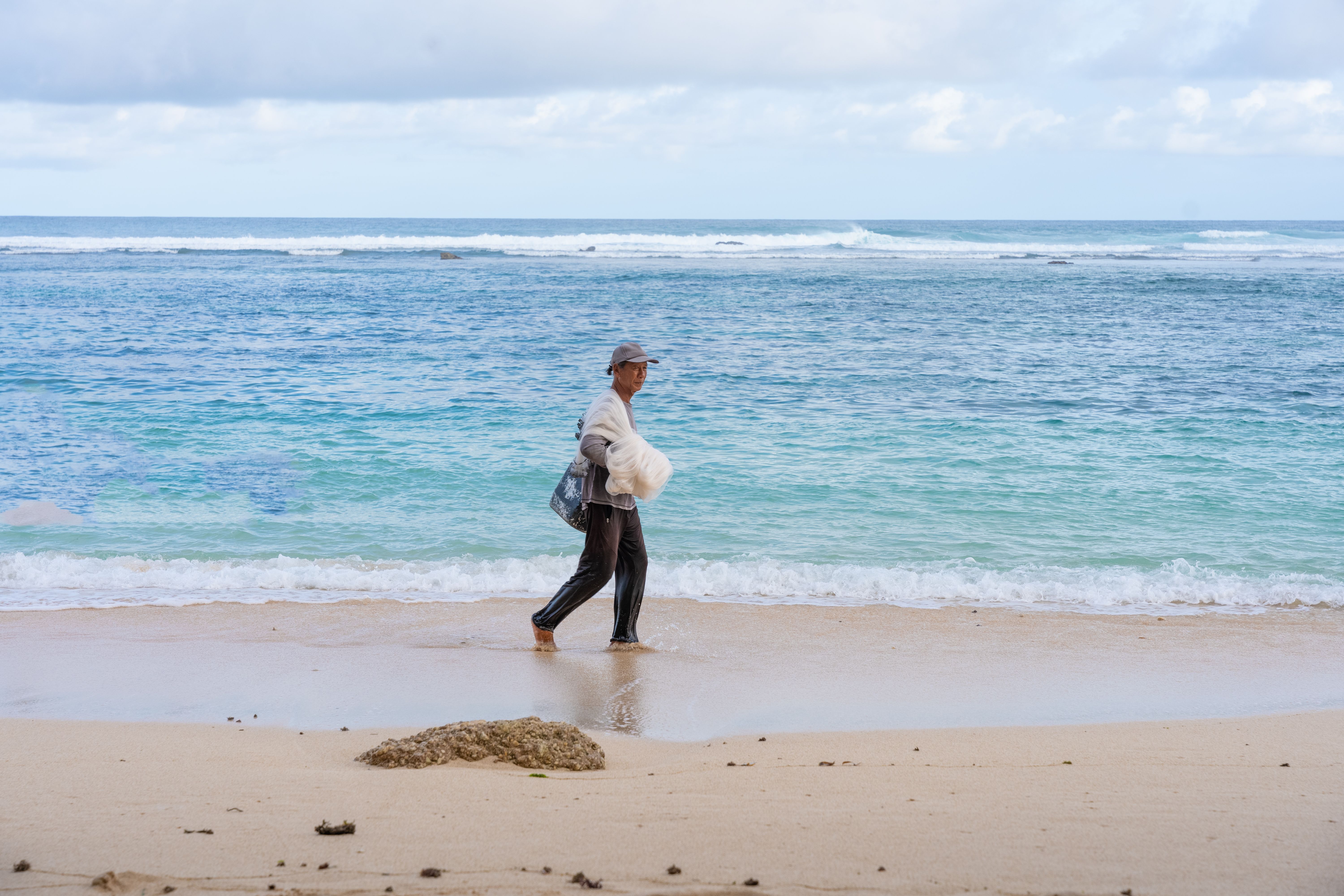 A serene scene of a man walking along a coastal beach, carrying a bag.