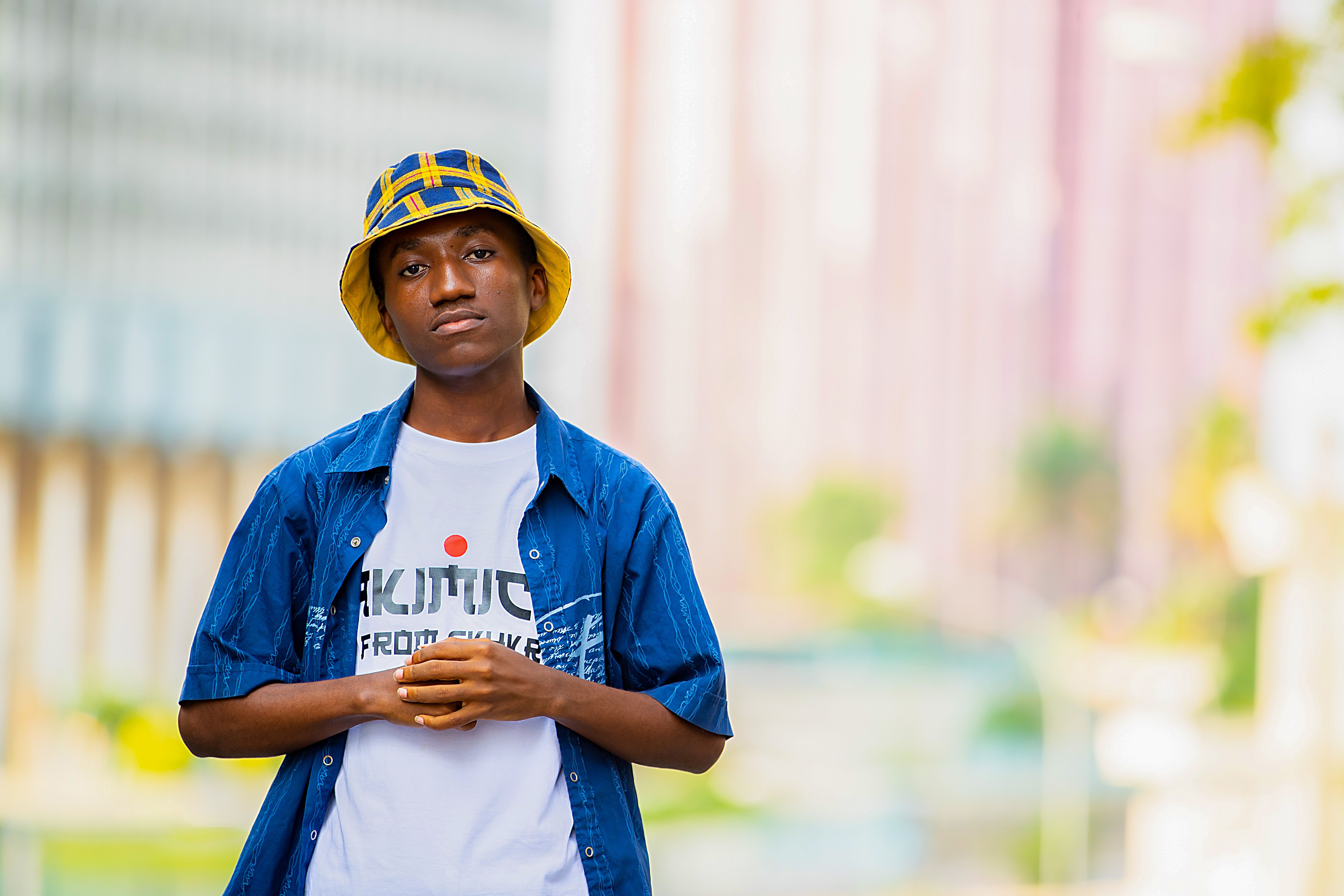 Young man in a blue shirt and bucket hat standing on a city street.