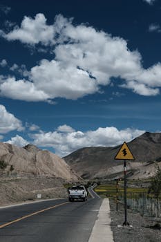 A vehicle travels a mountain highway under a dramatic sky, symbolizing adventure.
