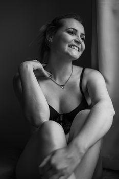 Stylish black and white portrait of a woman in lingerie, smiling and relaxed.