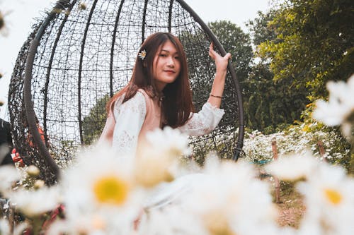 Woman Sitting on Bobble Chair Surrounded by Flowers Near Trees