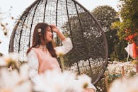 一位娴静的女子在鲜花盛开的花园里荡着柳条秋千，享受着阳光明媚的一天