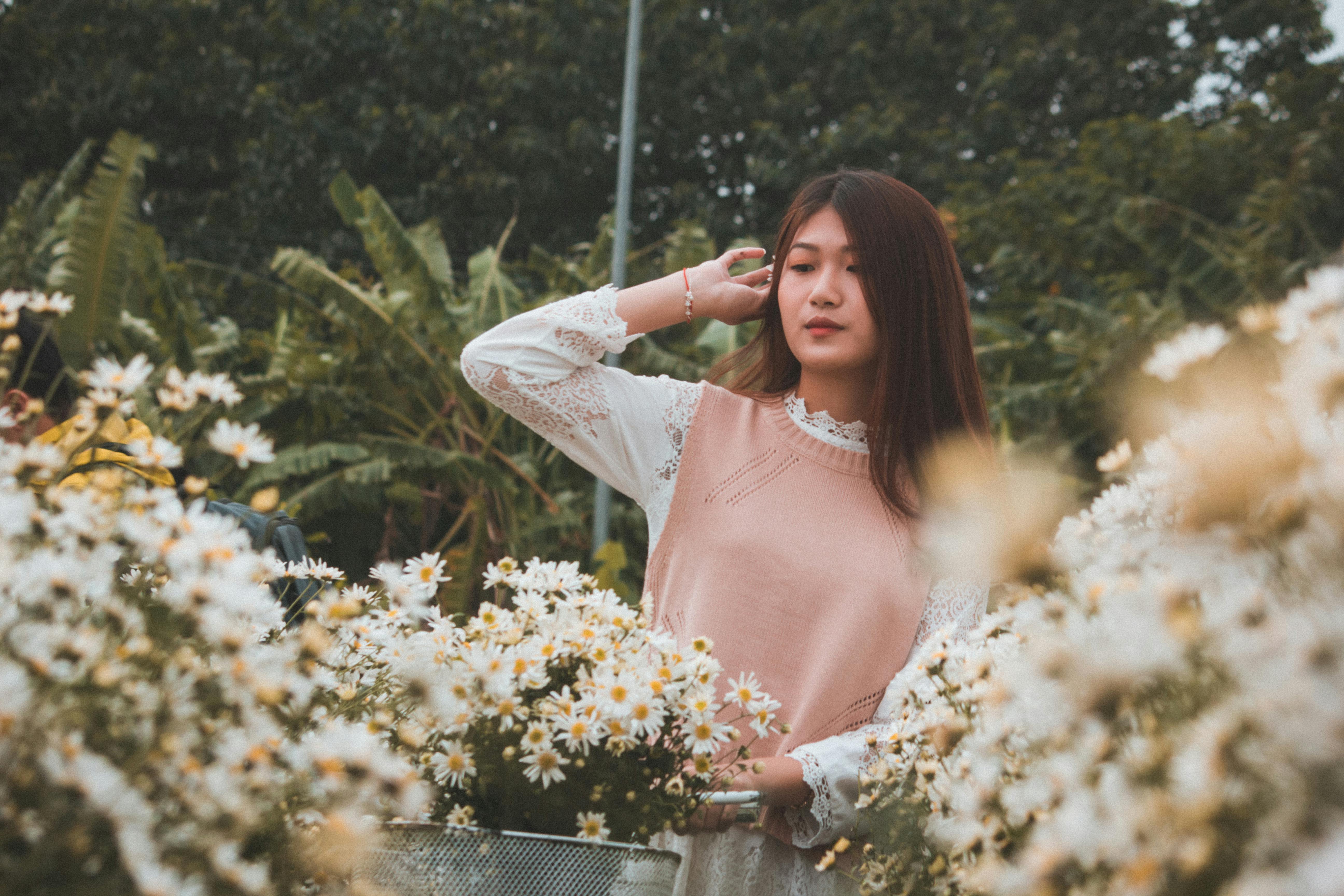 这幅宁静的肖像描绘了一位年轻女子站在花园里，周围是郁郁葱葱的白花