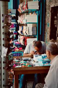 A shoe repair vendor working in Tripoli, Lebanon, with glasses displayed nearby.