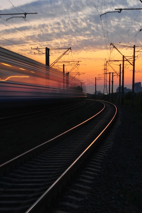 бесплатная Железная дорога под серым и оранжевым облачным небом во время заката Стоковое фото
