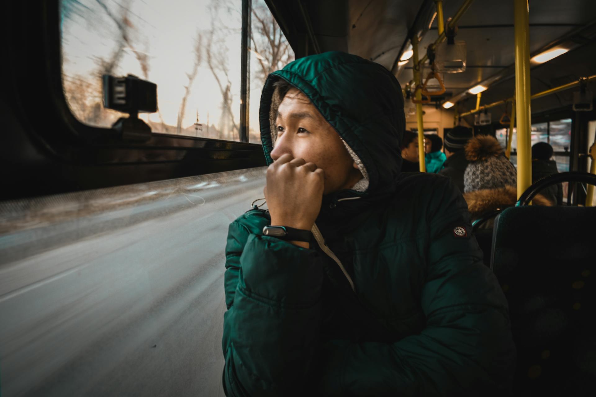 A thoughtful person in a jacket gazes out of a bus window, capturing the essence of travel.