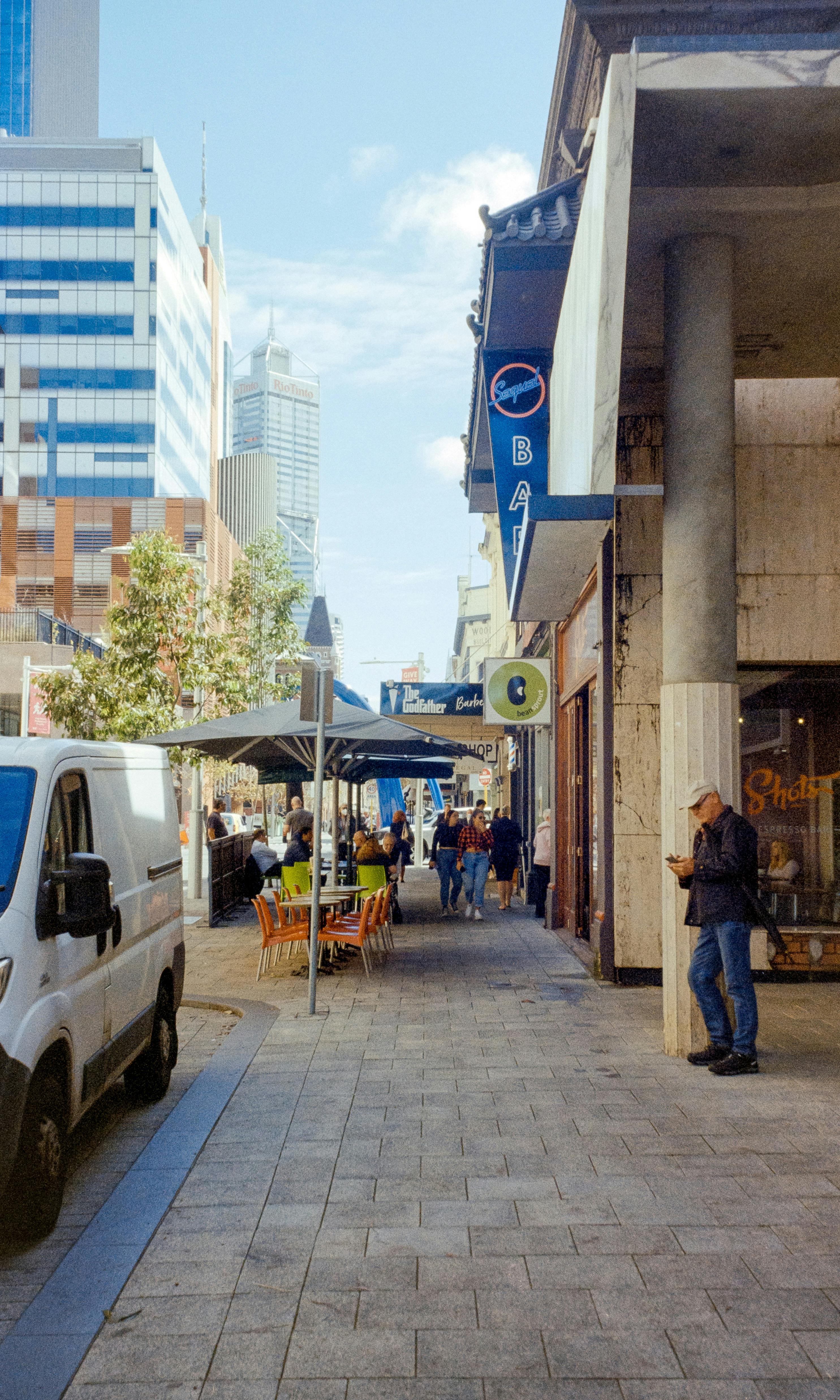 a city street with people walking and a van parked