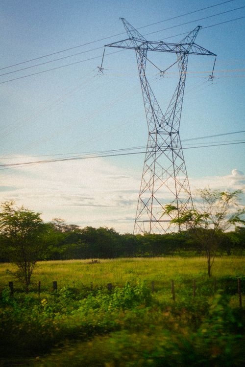 Free High voltage transmission tower in a lush green field under a bright sky, showcasing energy infrastructure. Stock Photo