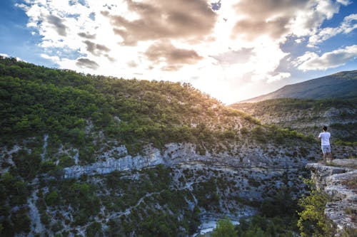 Uomo In Camicia Bianca In Piedi Sulla Cima Della Scogliera Di Montagna Sotto Le Nubi Cumuliformi