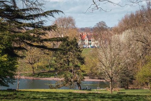 Free Scenic view of a lush park with a historic building in the background, surrounded by trees and a tranquil lake. Stock Photo