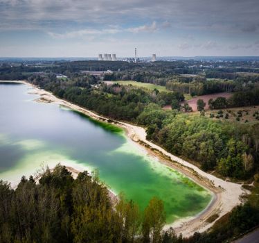 Drone shot of a vibrant green lake near Turek, Poland with a power plant visible in the background.
