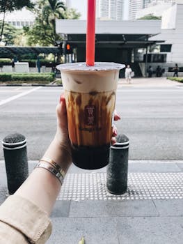 A person holding a cup of bubble tea with a cityscape background, taken outdoors.