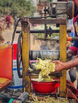 Close-up of a manual sugarcane machine in action at a bustling street market.