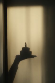 Mystical shadow of a hand holding a birthday cake on a sunlit wall, creating an artistic silhouette.