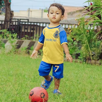 A young boy in sportswear playing soccer in a grassy backyard.