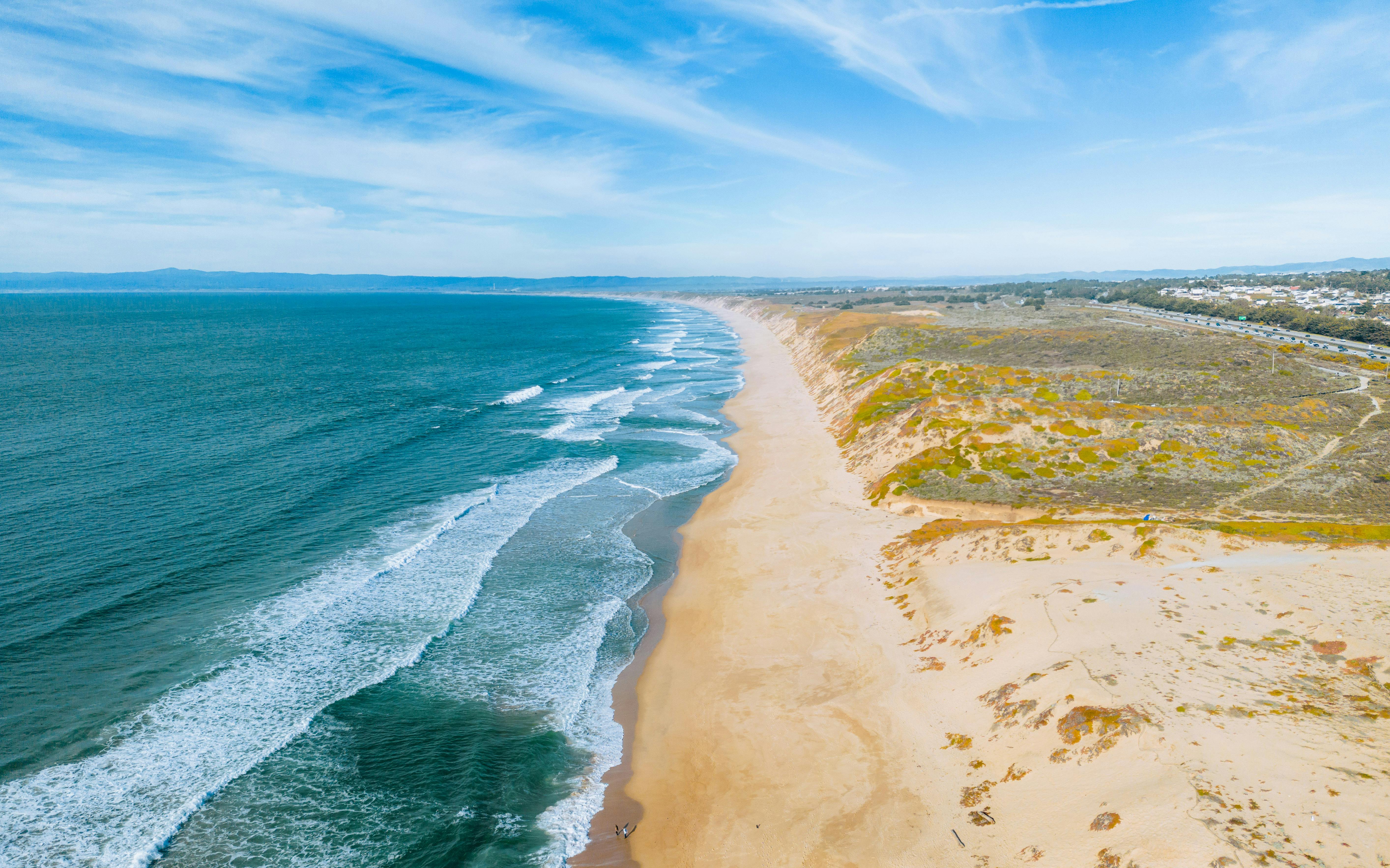 A breathtaking aerial view of a sandy beach and coastline under a bright blue sky, perfect for a summer getaway.