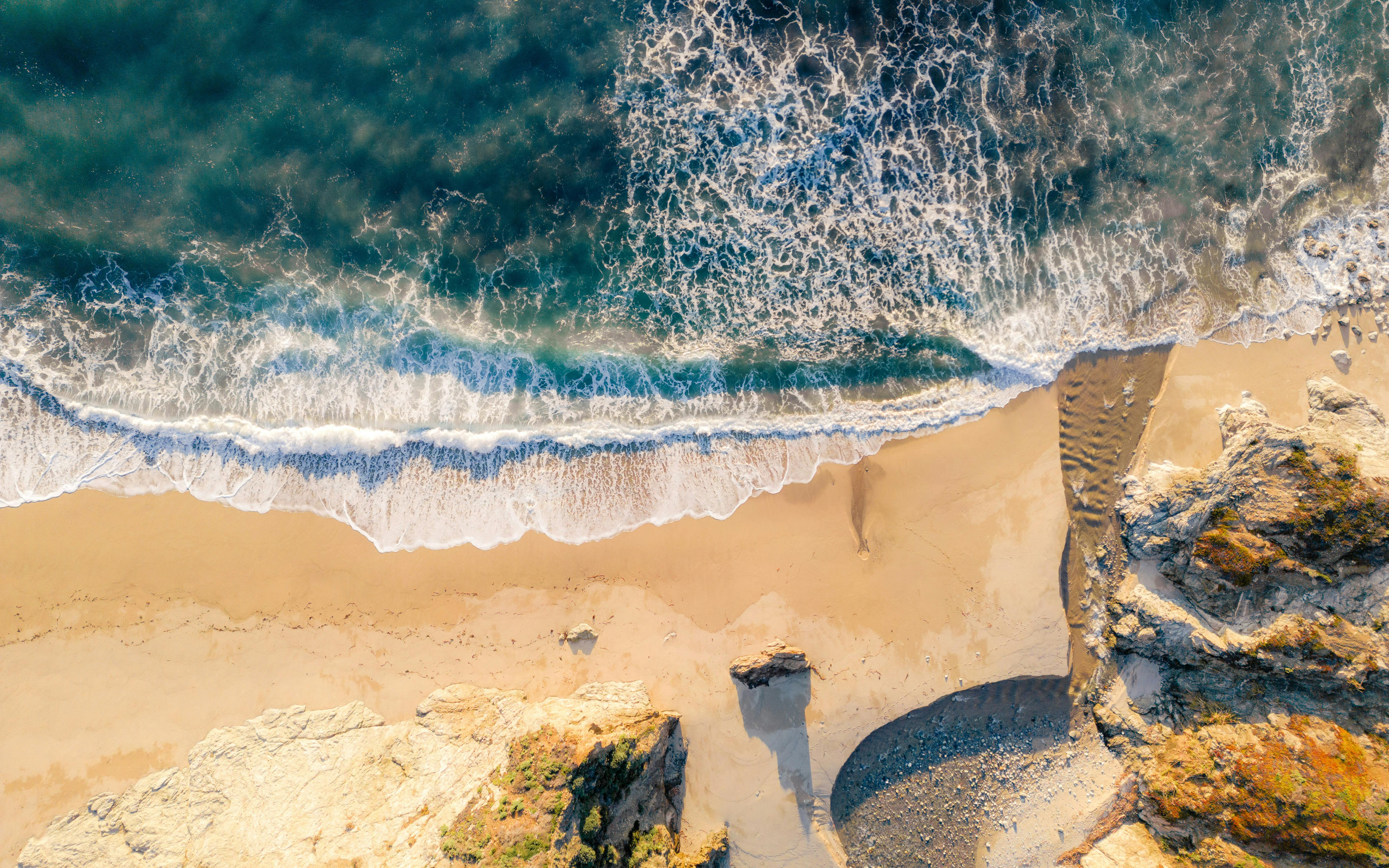 令人惊叹的海滩鸟瞰图，阳光下有汹涌的海浪、沙质海岸和岩石结构