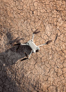 A white drone rests on cracked, arid ground, showcasing modern technology in a desolate setting.