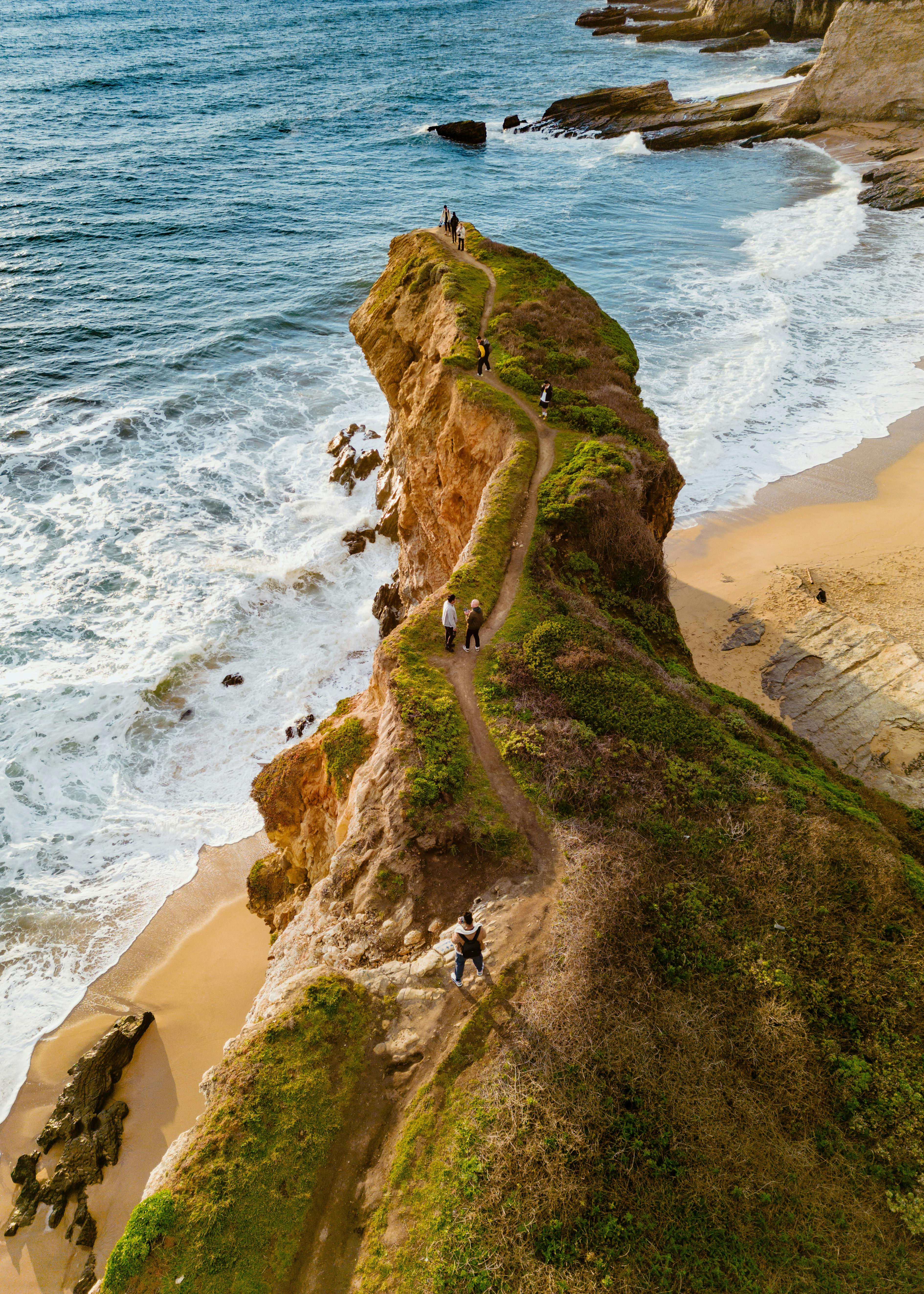 A breathtaking aerial view of people walking on a scenic coastal path along the ocean cliffs.
