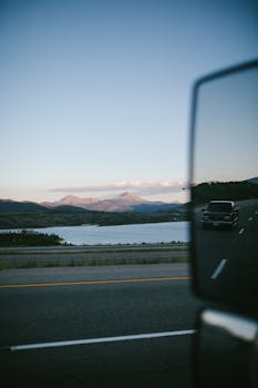 Car mirror reflection on a highway near a lake with mountain views in Colorado Springs.