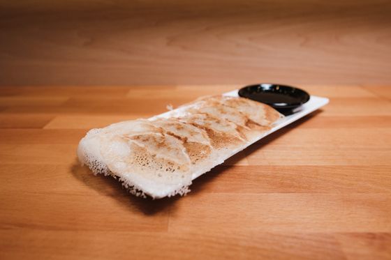 Row of pan-fried gyoza joined by a thin lacy crisp skirt on a white plate