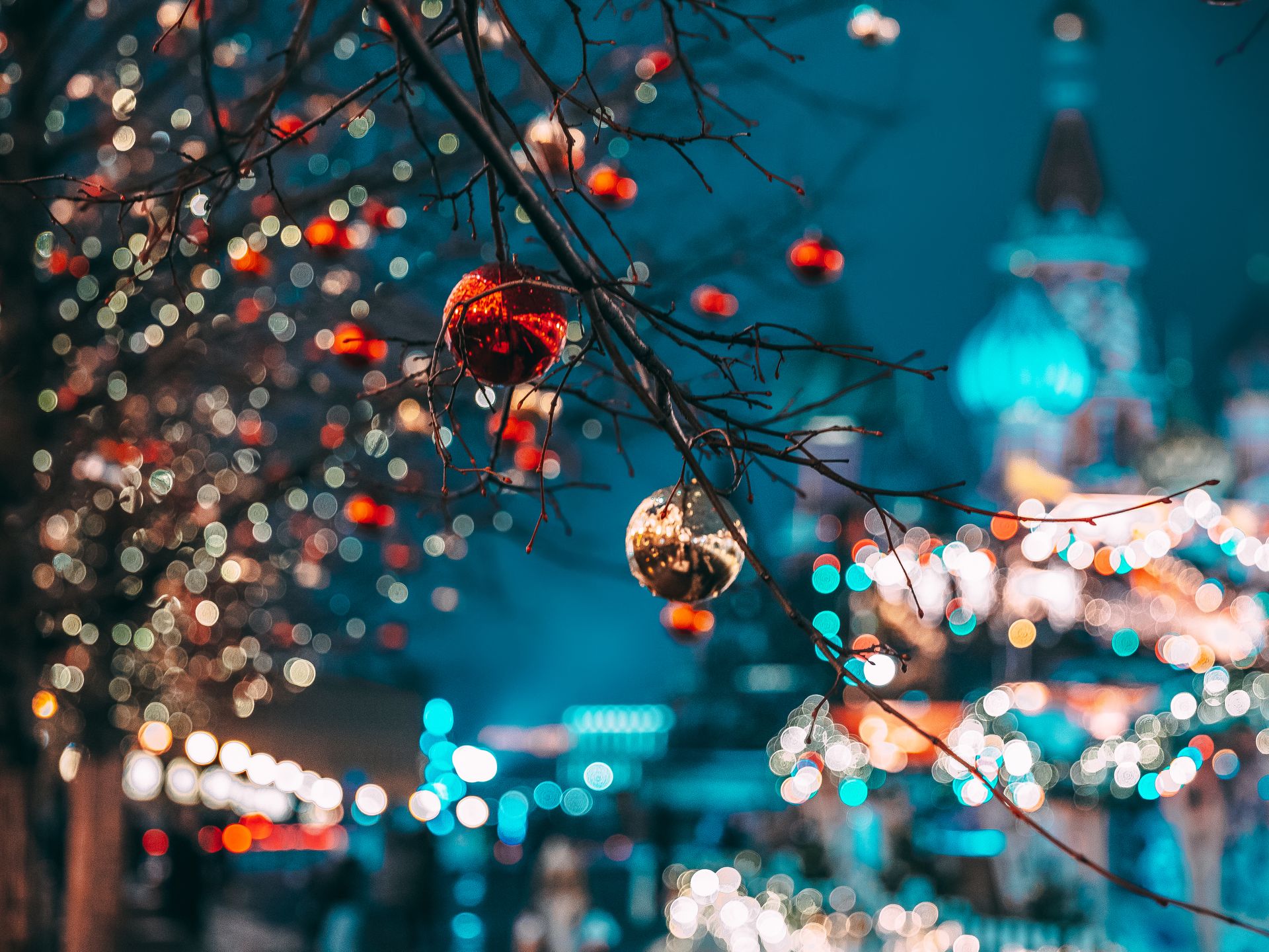 Close-up of Christmas ornaments hanging from tree branches with vibrant bokeh lights in the background.