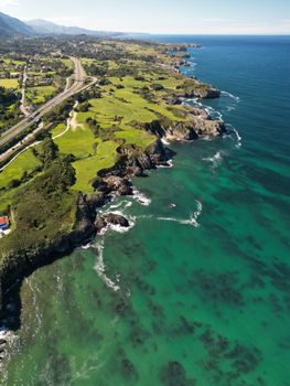 A stunning aerial view of the rugged coastline near Escamplero, Spain, showcasing lush greenery and vibrant blue waters.