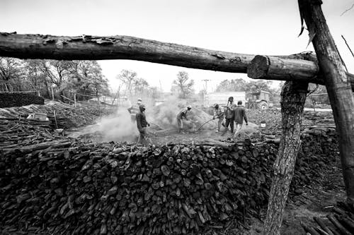 Black and white group of male workers with shovels around dusty pile during wood preparation