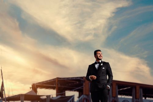 Free Stylish man in a tuxedo stands confidently against a sunset sky background. Stock Photo