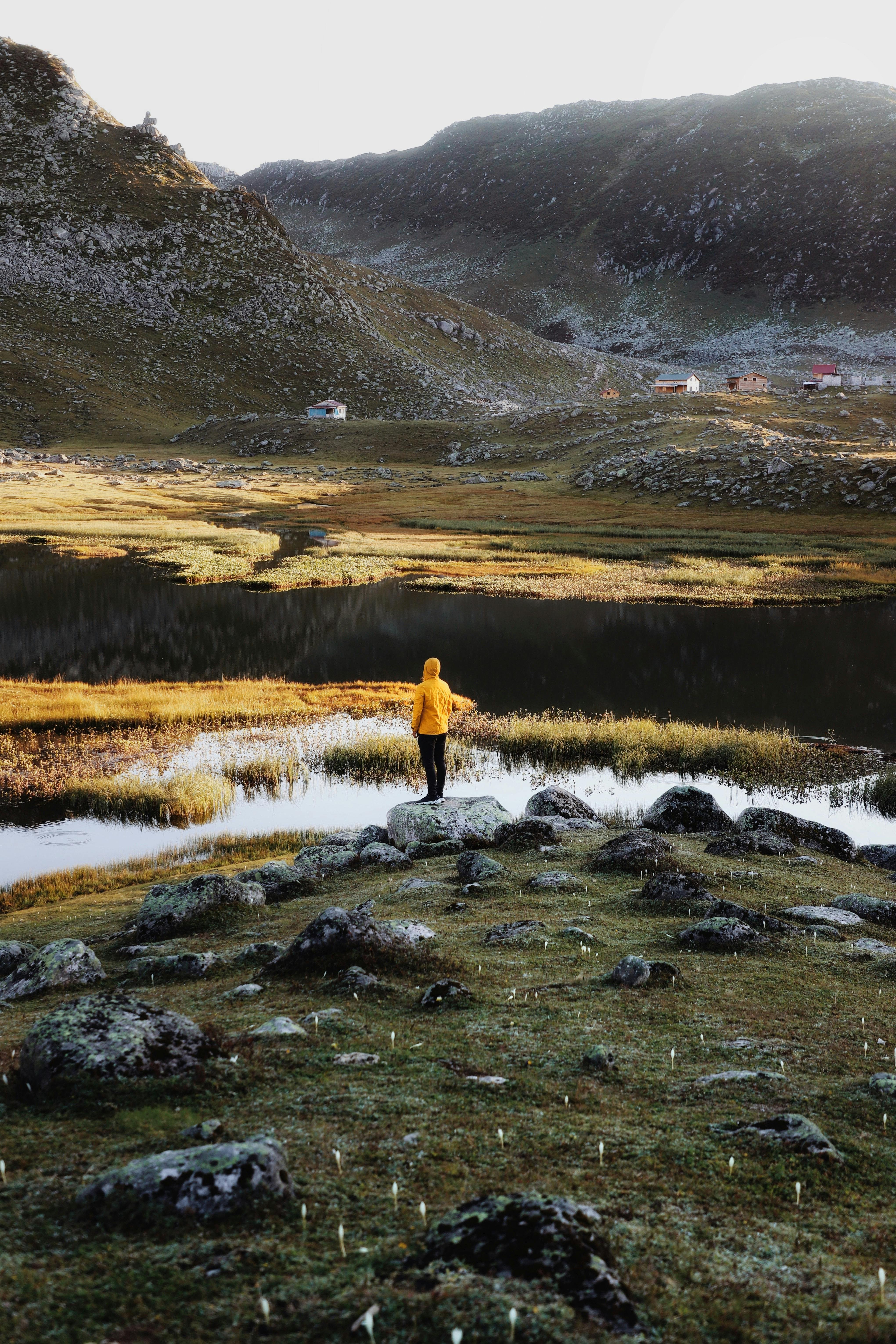 Person in yellow raincoat exploring serene mountain landscape by a lake.