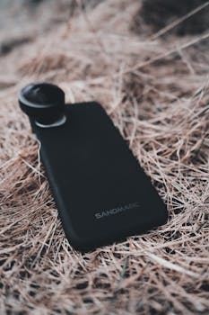 Close-up of a mobile phone with an attached lens lying on straw, highlighting modern technology.