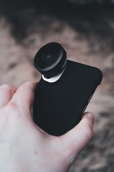 A close-up shot of a hand holding a smartphone with an attached fisheye lens.