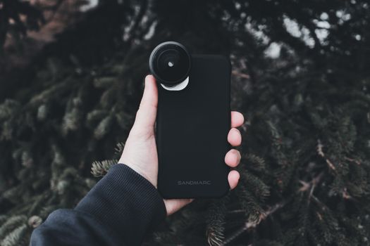 Close-up of a hand holding a smartphone with a fisheye lens, showcasing mobile photography technology.
