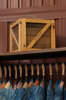 Close-up of a wooden crate labeled 'EXPORT' with denim jeans hanging below on leather straps.