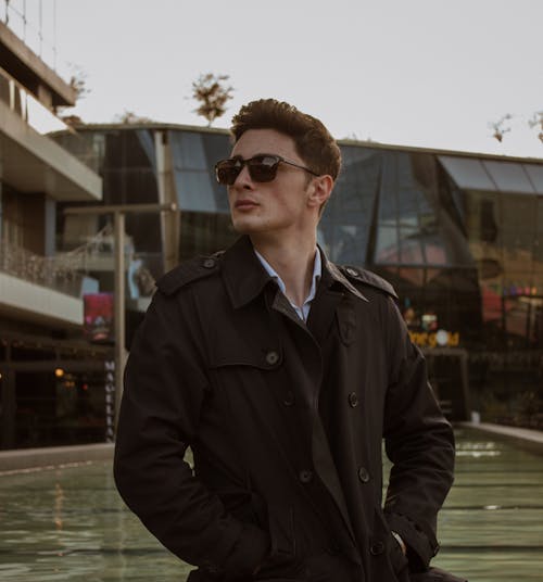 A man in a black coat and sunglasses standing next to a fountain