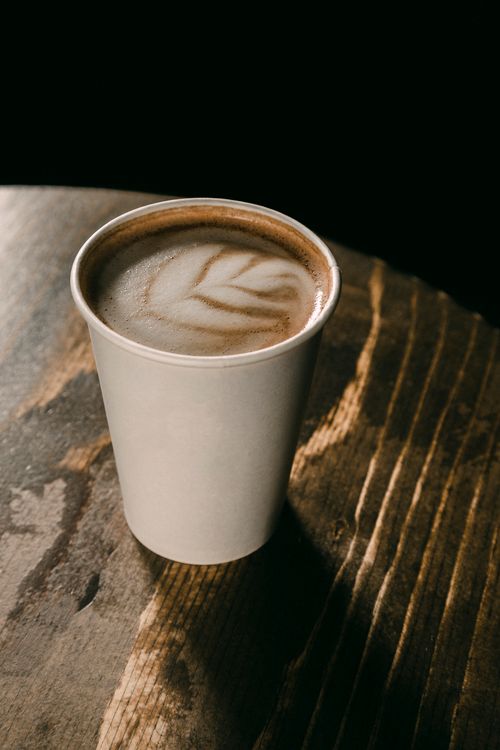 Free Close-up of a coffee with froth art in a paper cup on a rustic wooden table. Stock Photo