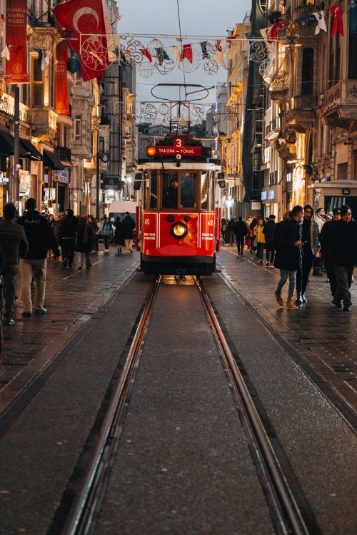 Free A red tram moves through bustling Istiklal Avenue, Istanbul, surrounded by historic architecture and evening lights. Stock Photo