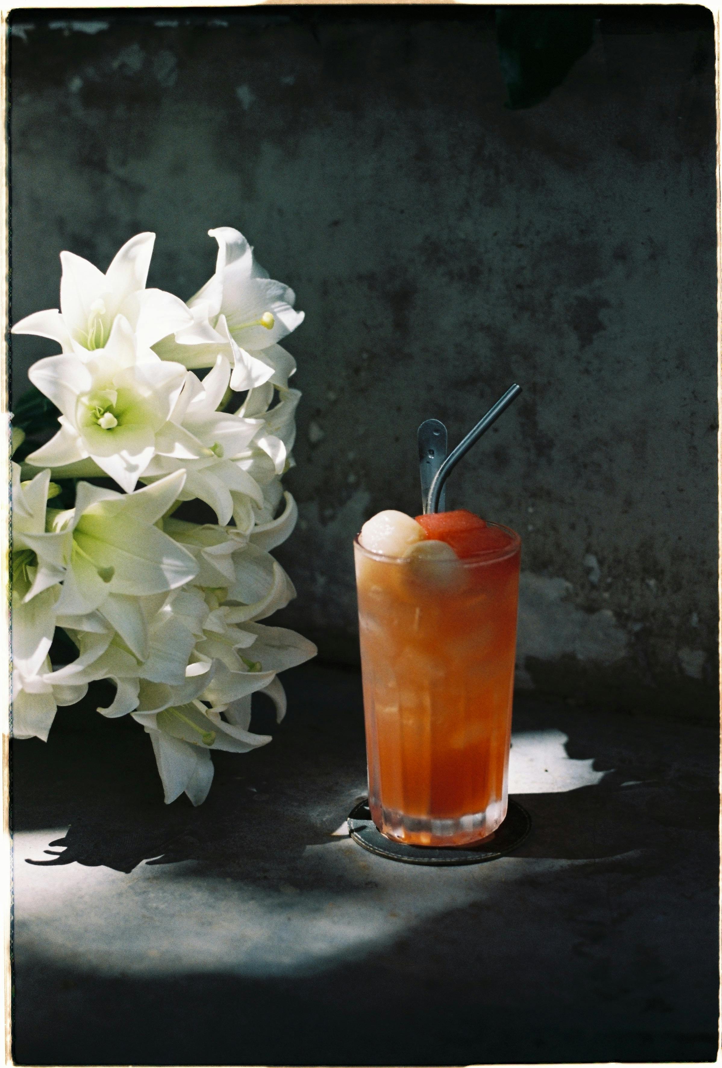 Chilled fruit drink with ice, accompanied by vibrant white lilies in natural lighting.