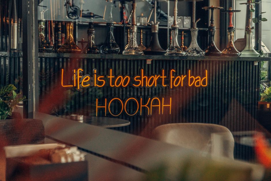 A neon sign reading Life is too short for bad HOOKAH in a chic hookah lounge representing hookah culture and equipment