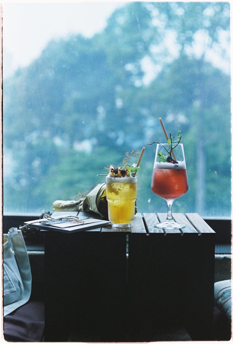 Glasses With Drinks On Wooden Table In Nature