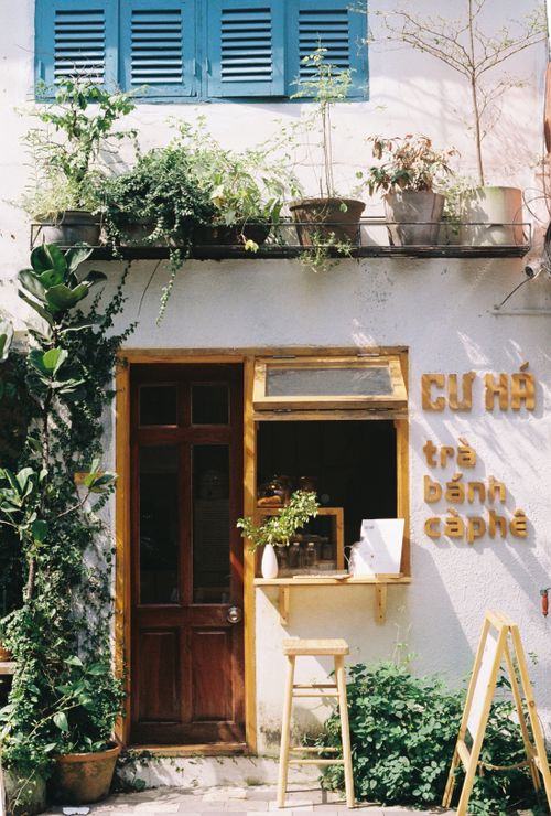 Free Cozy café exterior with lush plants and a welcoming wooden door, perfect for lifestyle and travel imagery. Stock Photo