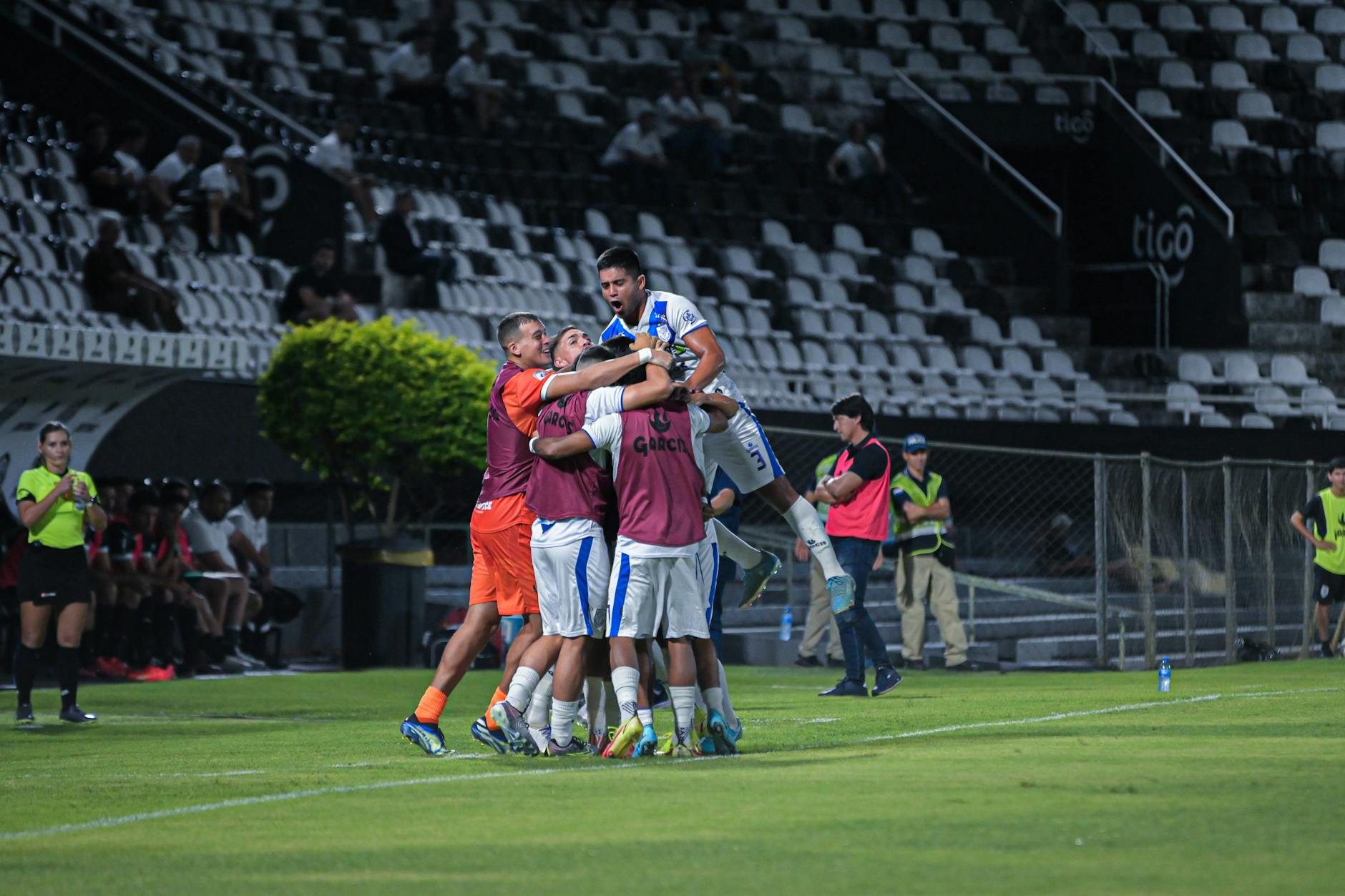 A soccer team celebrating a goal in an outdoor stadium during a night match.