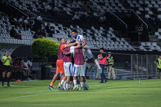 A soccer team celebrating a goal in an outdoor stadium during a night match.