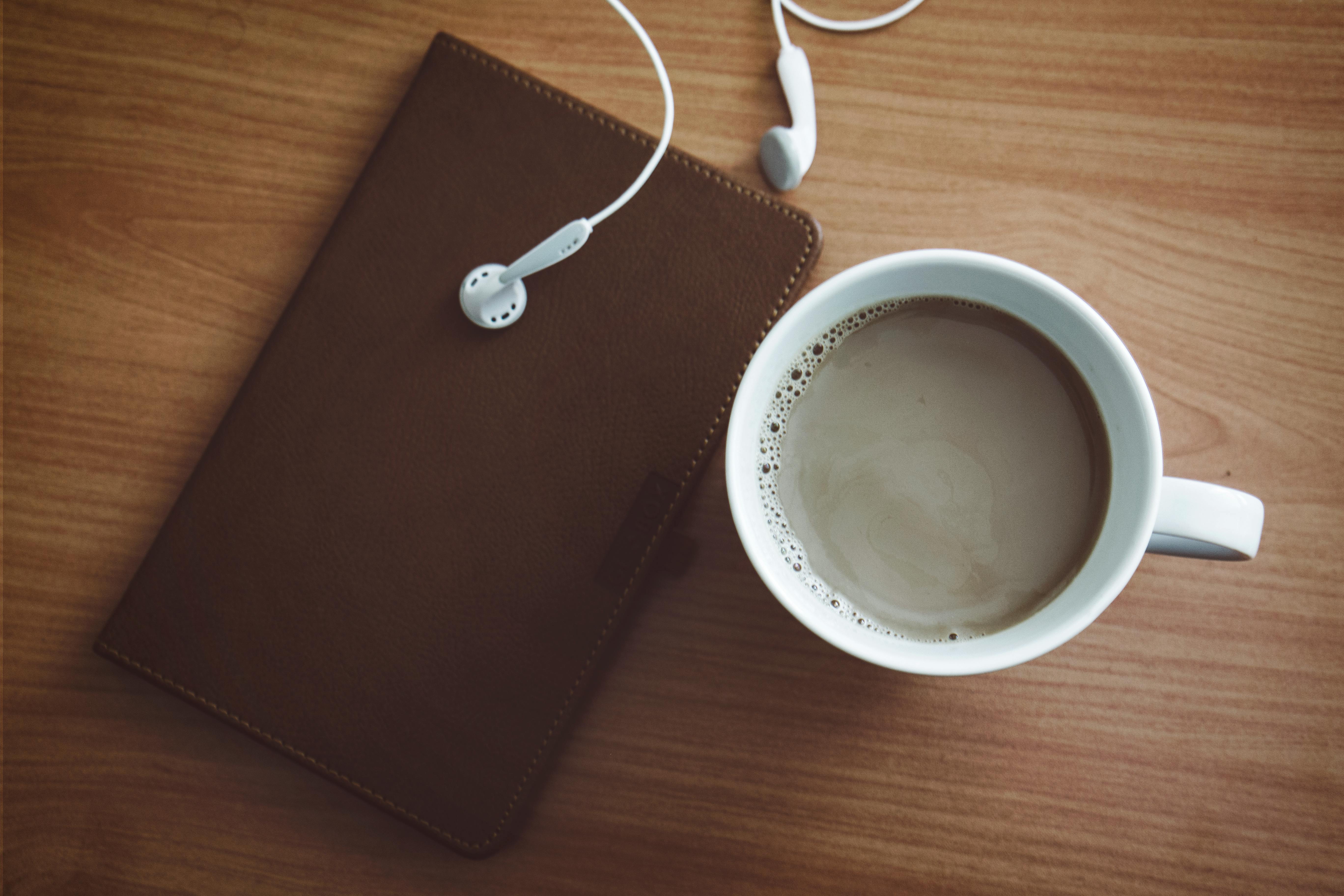 white mug beside wallet and earbuds