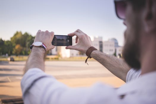 Tilt Shift Photo of Man Holding Black Smartphone Taking Photo of Gray Ground at Daytime