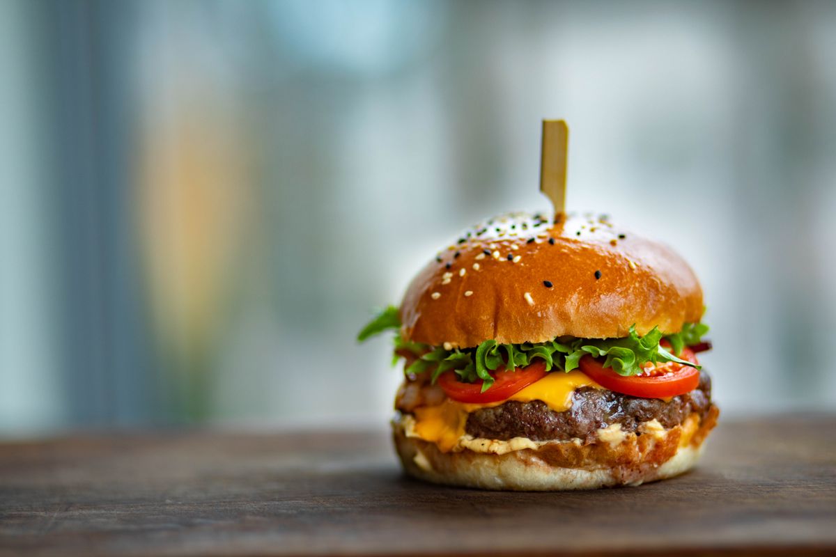Veganer Black-Bean-Burger mit selbstgemachtem Patty, frischen Tomaten und Burgersauce auf einem Holzbrett