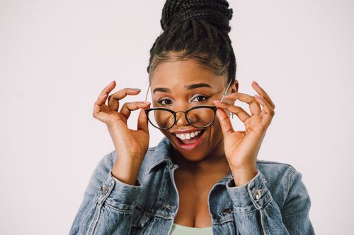 Free Smiling young woman in denim jacket adjusting her eyeglasses with excitement on a white background. Stock Photo