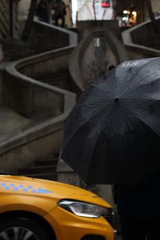 A rainy day scene in Istanbul with a yellow taxi and umbrella on a historic staircase.