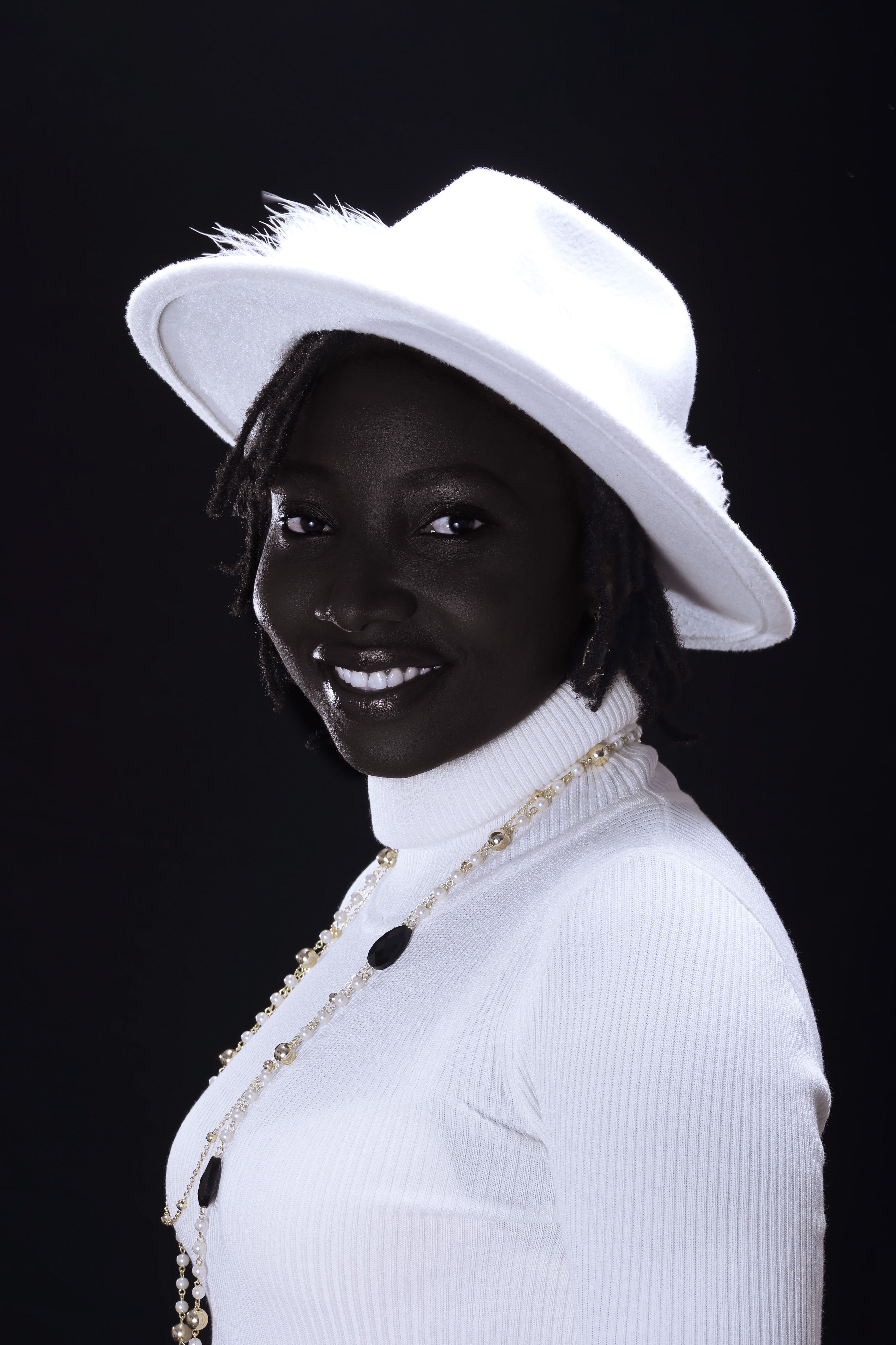A chic portrait of a smiling black woman in a white hat and clothing against a dark background, evoking style.