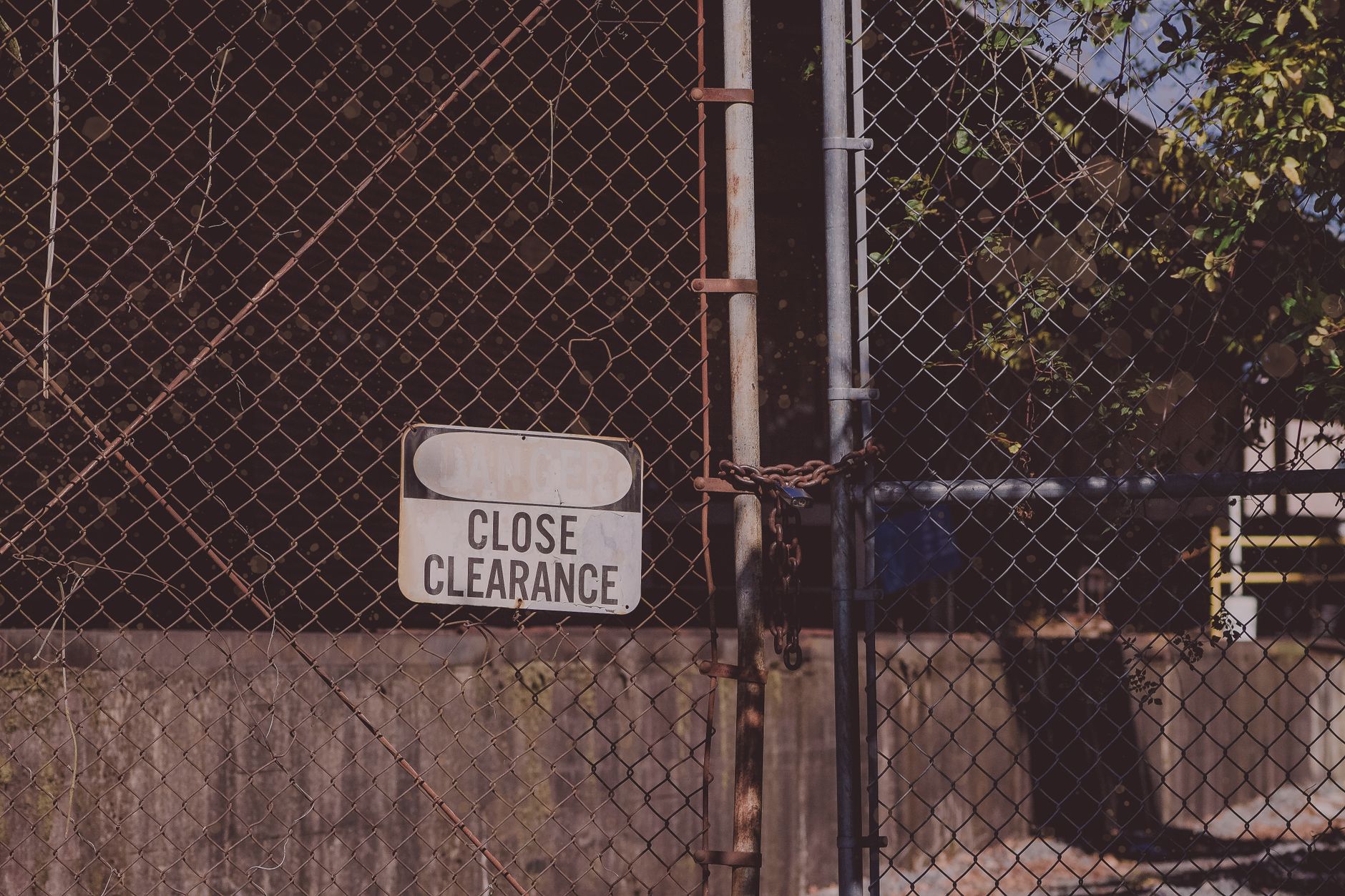 A rusty chain link fence with a 'Close Clearance' sign indicating security and safety measures.